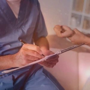 Nahaufnahme: Ein Physiotherapeut in blauer Berufskleidung notiert Therapieziele und Diagnostikdaten f&uuml;r eine Blankoverordnung auf einem Klemmbrett.